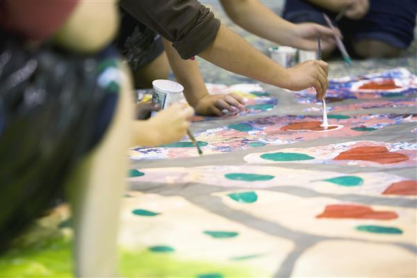 closeup of students painting on a large canvas